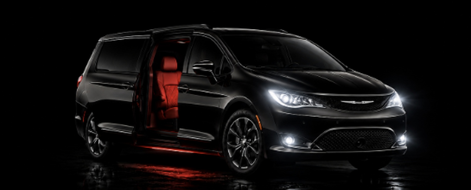 Black 2020-style minivan with headlights on and red interior visible through an open sliding door